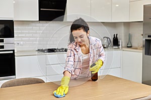 young woman cleaning wooden table with microfiber cloth.