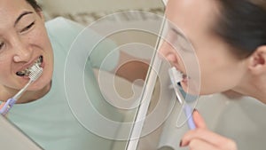 Young woman cleans braces with a brush, before mirror, top view.