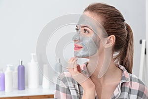 Young woman with cleansing mask on her face in bathroom. Skin care
