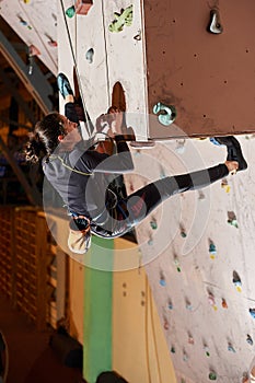 Young woman climbing up on practice wall in gym