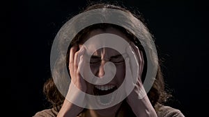 A young woman close-up screaming on black background. Mental illness concept.