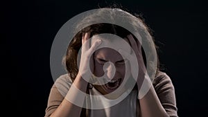 A young woman close-up screaming on black background. Mental illness concept.