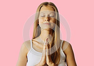 Young woman with closed eyes and hands in praying gesture. Meditation, balance and peace of mind concept. Isolated over pink