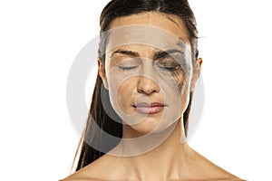 A young woman with closed eyes posing with half face dirty and half cleansed of makeup on a white background photo