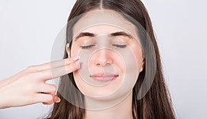 Young woman with closed eyes spreads moisturizing cream on her face. Skincare cosmetics, beauty spa procedures concept