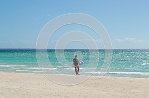 Young woman in closed swimsuit with swimming circle undressing on sand deserted beach