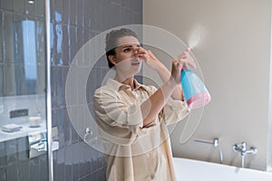 A young woman closing her nose from unpleasant smell and spraying air freshener