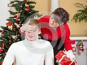 Young woman closing man eyes by her hands with gift