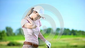 Young woman with club playing golf, suffering sharp shoulder pain, sports trauma