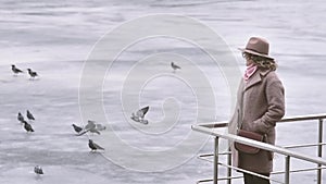 Young woman in coat by a frozen lake with birds