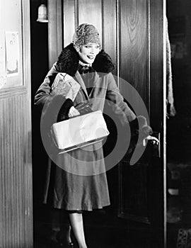 Young woman in a coat and hat entering into a room