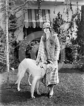 Young woman in coat and hat standing outside with her Russian Wolfhound