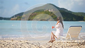 Young woman with cocktail glass on white beach sitting on sunbed