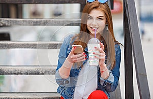 Young woman with a cocktail , reading a text message on the street