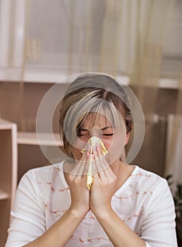 Young woman with cold blowing her runny nose.