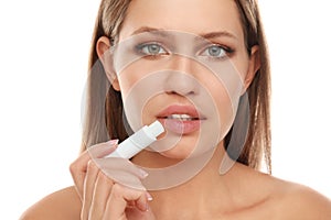 Young woman with cold sore applying lip balm against background