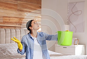 Young woman collecting leaking water from ceiling in bedroom. Time to call roof repair service