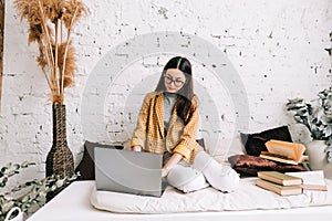 Young woman college student in eyeglasses studying with laptop, distantly preparing for test exam, doing homework at home, photo