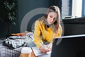 Young woman college student studying with laptop, distantly preparing for test exam, writing essay doing homework at home, photo