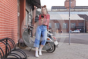 Young woman with colored pigtails using mobile phone on moped