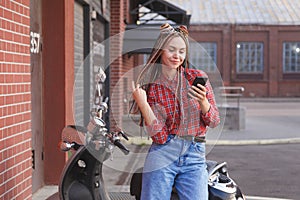 Young woman with colored pigtails using mobile phone on moped