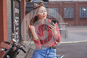 Young woman with colored pigtails using mobile phone on moped