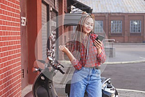 Young woman with colored pigtails using mobile phone on moped