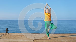A young woman in colorful clothes practices yoga by the sea or ocean.