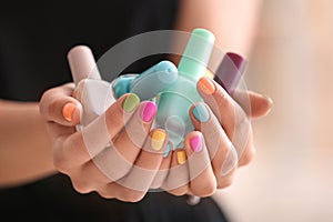 Young woman with colorful manicure holding bottles of nail polishes, closeup