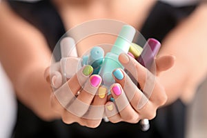 Young woman with colorful manicure holding bottles of nail polishes, closeup