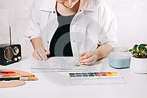 Young woman coloring page antistress at table indoors, mental wellbeing and art therapy. Woman paints a sketch by paintbrush,