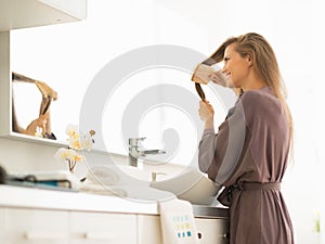 Young woman combing hair in bathroom