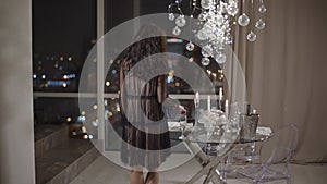Young woman comes to the window with a spectacular view of a night city.