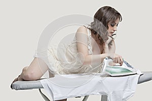 Young woman comfortably ironing shirt against gray background photo
