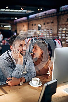 Blurred faces of young man and woman colleagues talking in front of table with desktop computer, in clothing store