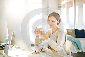 A young woman with computer and smartphone indoors, working in a home office.