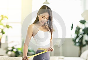 A young woman at home confidently measured her waist circumference, satisfied with her posture, and very happy to lose weight photo