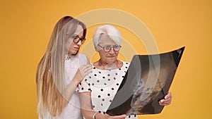 Young woman confronting worried senior lady holding a x-ray o MRI head scan