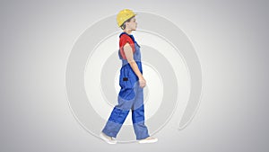 Young woman construction worker in yellow hardhat walking on gradient background.