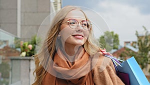 Young woman consumer smiling enjoying weekends girl shopaholic walking outdoors after shopping caucasian female rejoices