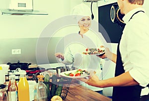 Young woman cook giving salad to waitress