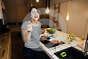 Young woman cooking a healthy meal in home kitchen.Making dinner on kitchen island standing by induction hob.Preparing fresh