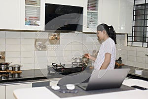 Young woman cooking in the kitchen at home using her laptop computer