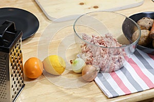 Young woman cooking in kitchen. Housewife preparing vegetables for cooking. Fresh potatoes, onions, meat, lemon and mushrooms.