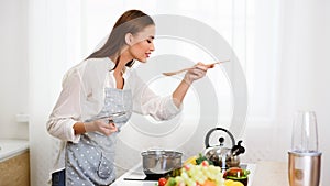 Young Woman Cooking Soup And Tasting From Spoon