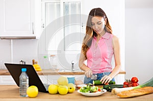 Young woman cooking vegetables for dinner and browsing sns on laptop