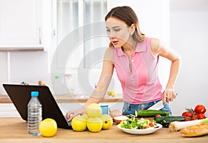 Young woman cooking vegetables for dinner and browsing sns on laptop