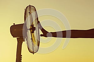 Young Woman cooling herself during hot weather in front of fan on a blue sunset sky background