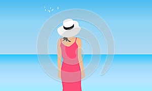 Young woman in coral dress and white hat stands on background of blue sea and sky