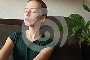 Young woman with a cosmetic mask on her face in green t-short. Applying face mask of clay at home.